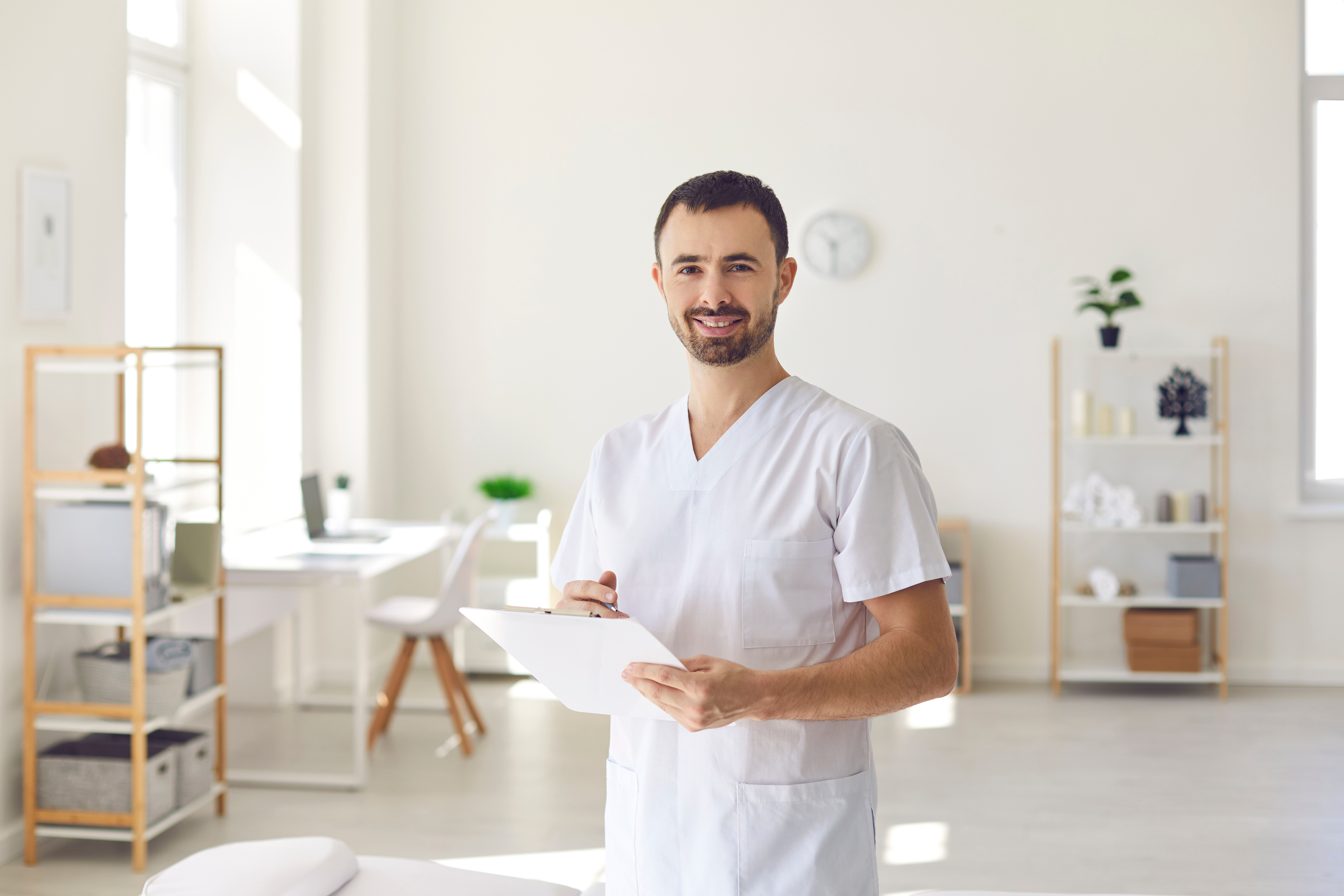 Smiling Man Doctor Chiropractor or Osteopath Standing with Notes and Looking at Camera